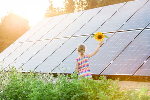 Kind läuft mit einer Sonnenblume in der Hand vor einer Solaranlage